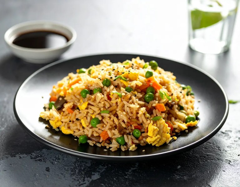 Gebratener Reis mit Gemüse, Ei und Sesam, serviert auf einem dunklen Teller mit Essstäbchen – asiatisches Gericht auf rustikalem Holztisch, seitlich beleuchtet durch natürliches Tageslicht. Rezept auf Dilos Kitchen | diloskitchen.com